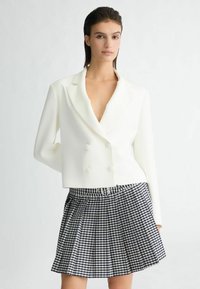 Witte gecroppte dubbele blazer met een diepe V-hals en lange mouwen, gecombineerd met een marineblauw en wit geruit plissérok.
