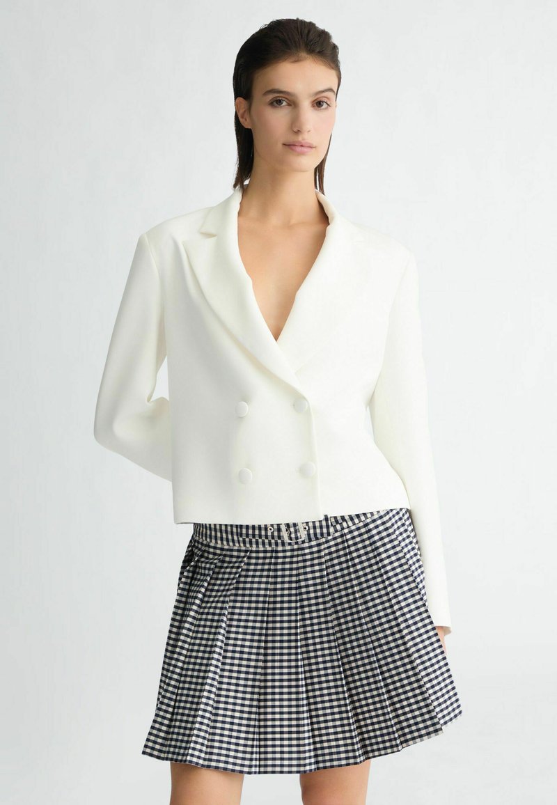 Witte gecroppte dubbele blazer met een diepe V-hals en lange mouwen, gecombineerd met een marineblauw en wit geruit plissérok.