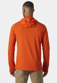 Koszulka z długim rękawem i kapturem w intensywnym pomarańczowym kolorze, wykonana z teksturowanej tkaniny o subtelnych wzorach, charakteryzująca się luźnym krojem i wydłużonymi rękawami.