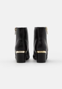 Botas de tobillo de cuero negro con cierre de cremallera, con un tacón cuadrado acentuado en dorado y un detalle del logo en la base del tacón.