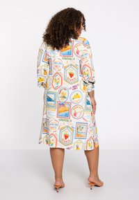 Kurzärmliges Kleid aus leichtem Stoff, mit einem bunten reiseme-themed Druck und hexagonalen Rahmen, vornehmlich auf weißem Hintergrund.