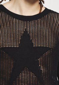 Schwarzer gestrickterPullover mit einem offenen Maschenmuster und einem großen schwarzen Sternmuster in der Mitte. Rundhalsausschnitt und strukturierter Stoff.