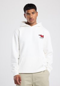 Sudadera blanca con un bolsillo tipo canguro, con un gráfico y logo rojo bordado en el pecho. Tejido suave con puños y dobladillo acanalados.