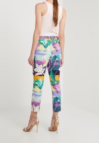 Kolorowe spodnie w kwiatowy wzór z odcieniami zieleni, fioletu i żółci, zestawione z metalicznymi, złotymi sandałami na wysokim obcasie.