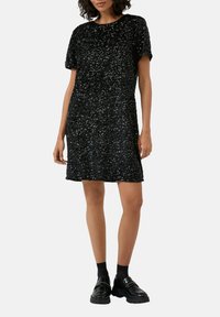 Czarna sukienka z cekinami, o okrągłym dekolcie i krótkich rękawach, cechująca się luźnym krojem i teksturowaną powierzchnią. Do tego czarne mokasyny.
