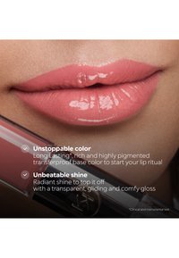 Glossy pink lips with a transparent lip gloss applicator held near the lower lip, showcasing long-lasting color and radiant shine.