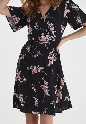 Vestido negro cruzado con estampados florales en rosa y blanco, mangas cortas acampanadas y detalle de lazo en la cintura.