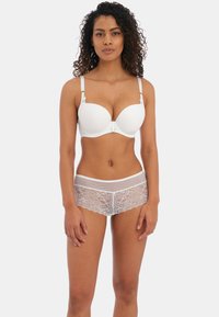 Witte gewatteerde beha met verstelbare banden en een centrale sluiting, gecombineerd met witte kant boyshorts met een bloemenpatroon.