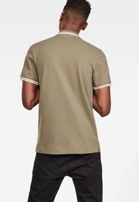 Polo en kaki à manches courtes, avec des accents de rayure blanche sur le col et les manches, fabriqué à partir d'un tissu doux en mélange de coton.