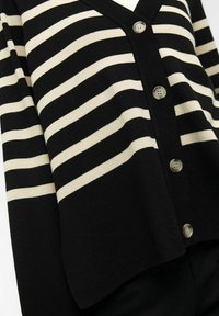 Cardigan a righe nero e crema con scollatura a V, cinque bottoni e polsini a costine. Tessuto lavorato a maglia con texture liscia.
