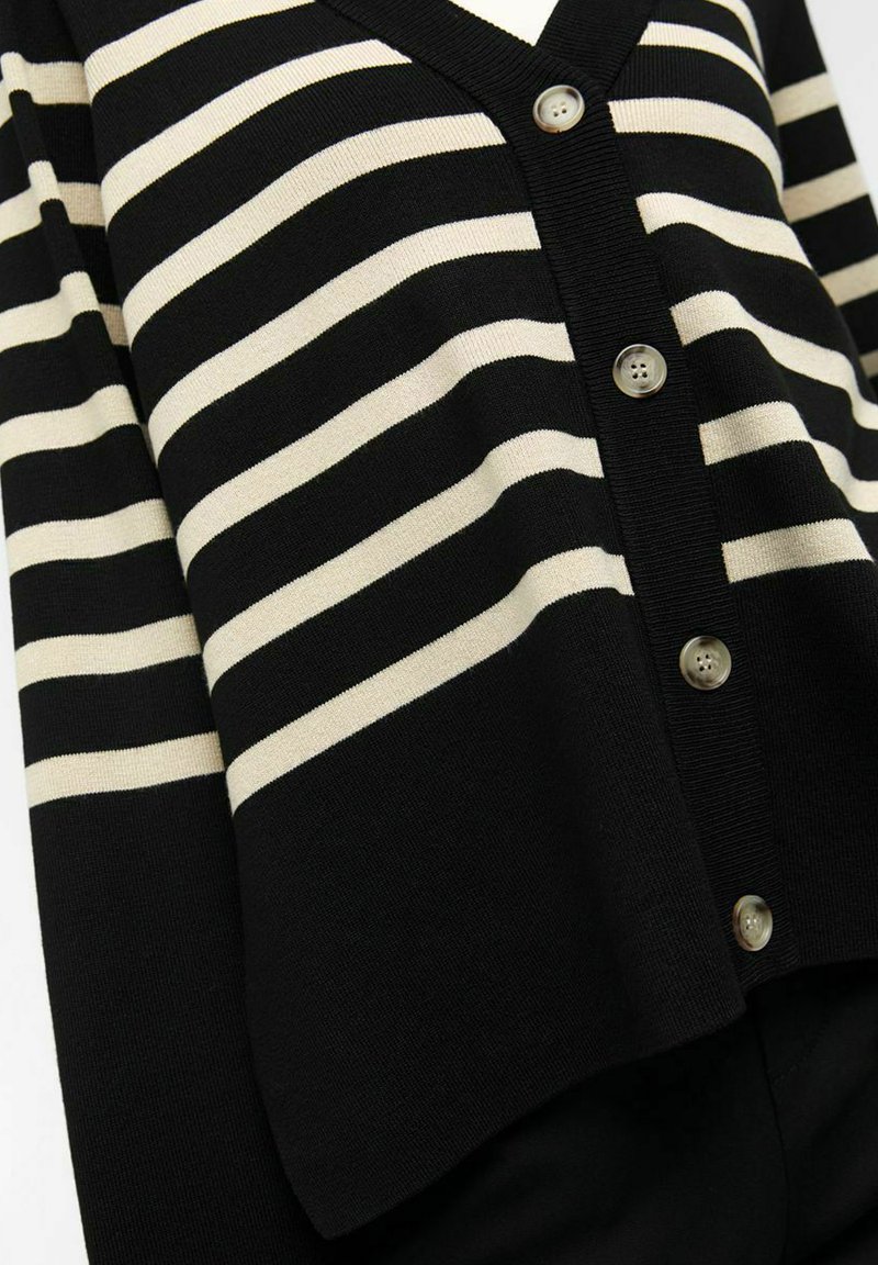 Cardigan rayé noir et crème avec un col en V, cinq boutons et des poignets côtelés. Tissu tricoté avec une texture lisse.