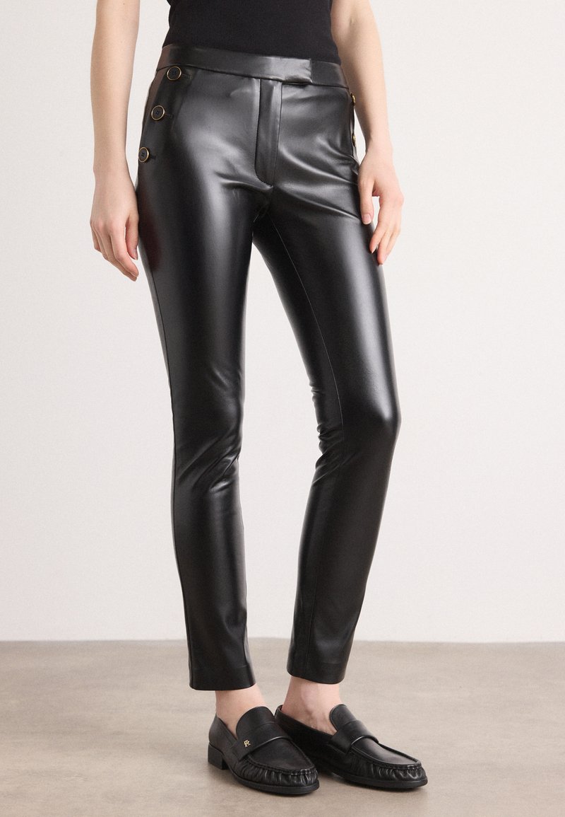 Mustat tekonahkahousut, joissa on slim fit -leikkaus, kiiltävä pinta, sivuvetoketju ja kolme koristeellista kultahermosta vyötäröllä.