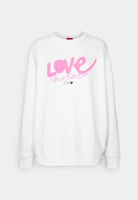 Sudadera blanca de manga larga, con un gráfico rosa que dice "AMOR" sobre "a ti mismo" y un pequeño ícono de corazón negro debajo.