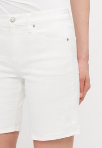 Hvite denimshorts har en tettsittende design med glidelås, fem lommer og subtile detaljer i sølvmetall.