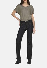 Top corto metallico verde oliva abbinato a jeans blu scuro e stivali neri alla caviglia. L'outfit presenta una vestibilità comoda e una finitura satinata.