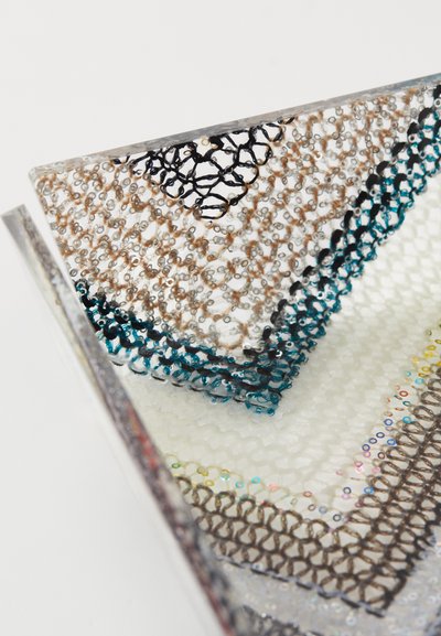 Pochette transparente avec un design textile en sequins multicolores, présentant des coutures bleues, noires et beiges ; forme structurée et angulaire.