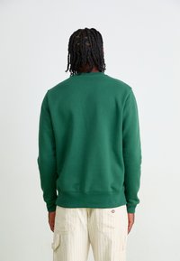 Green sweatshirt with a round neckline, ribbed cuffs, and hem. The fabric appears soft and textured, featuring a clean, solid design.