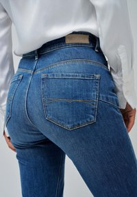 Jeans in denim blu caratterizzati da una silhouette aderente, due tasche posteriori con cuciture curve e un'etichetta in pelle con il marchio sulla vita.
