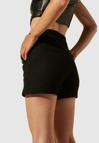 Shorts noirs texturés avec une coupe ajustée. Ils présentent une taille haute et des poches latérales. Le tissu a un motif tissé. Aucun matériel visible.