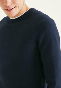 Pull bleu marine en tissu tricoté texturé, avec un col rond et des accents côtelés sur les épaules et le col.