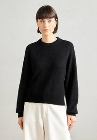 Black knit sweater with a round neck, long sleeves, and ribbed hem. The fabric has a soft, fuzzy texture and a relaxed fit.