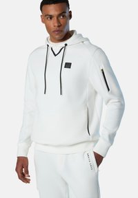 Felpa bianca con cappuccio, dotata di un patch logo nero, laccetti e tasca laterale con zip. Presenta una vestibilità rilassata e polsini a costine.