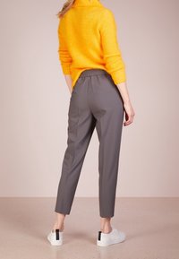 Pantalon gris à coupe fuselée avec taille élastique, associé à un pull en maille jaune vif et des baskets blanches avec des accents noirs.