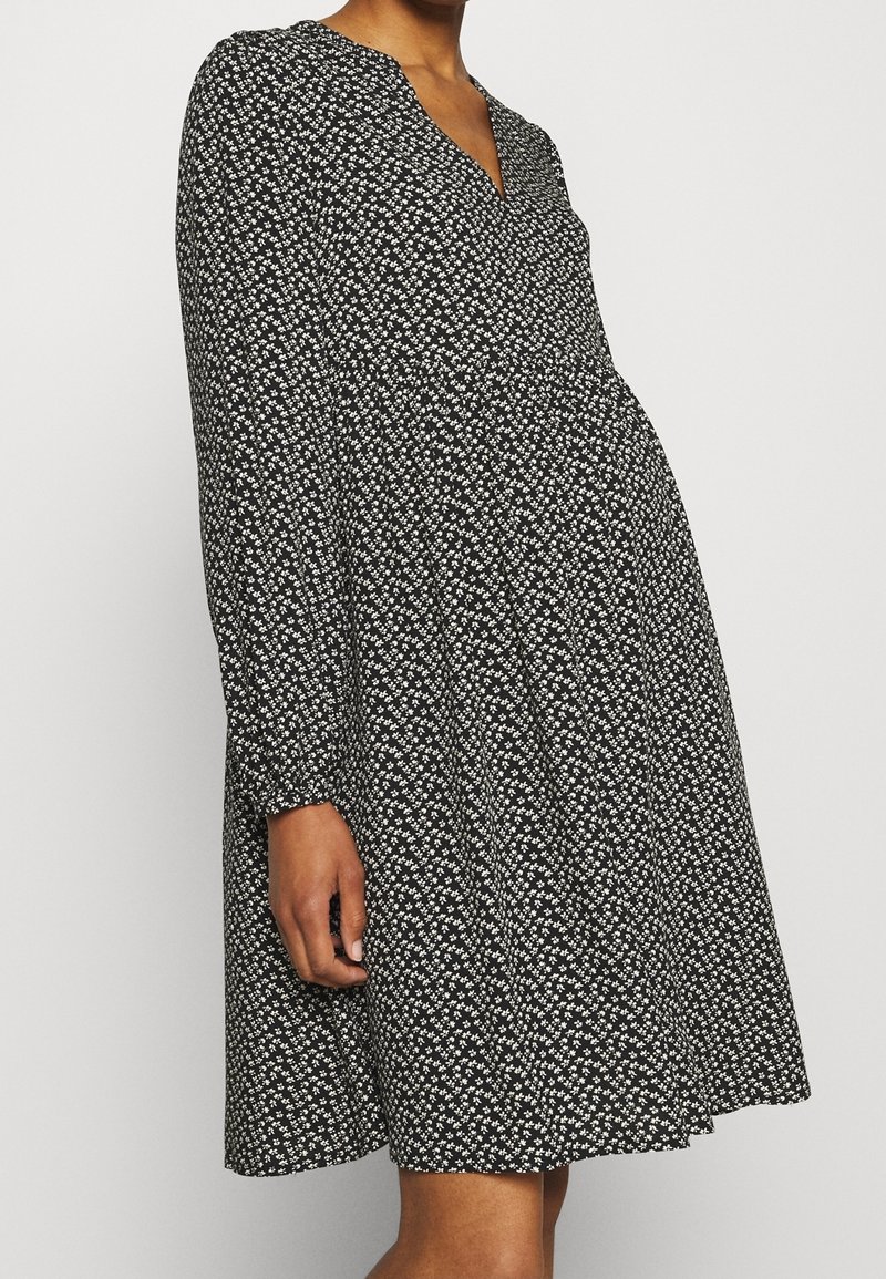 Robe noire à manches longues, col en V, avec un motif floral blanc. Silhouette évasée avec une taille froncée, confectionnée dans un tissu léger.