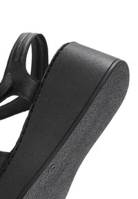 Sandale à plateforme noire avec une tige en cuir lisse et une semelle en caoutchouc texturé. Le design comprend des découpes et des accents cousus.