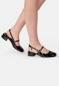 Fekete lakk bőr slingback cipők négyzetes orral, állítható bokaheggyel és alacsony tömbsarokkal. Texturált, fényes felület.