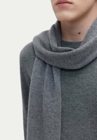 Grå ullscarf hängande runt halsen, med mjuk textur och slät yta, i kombination med en liknande grå tröja.