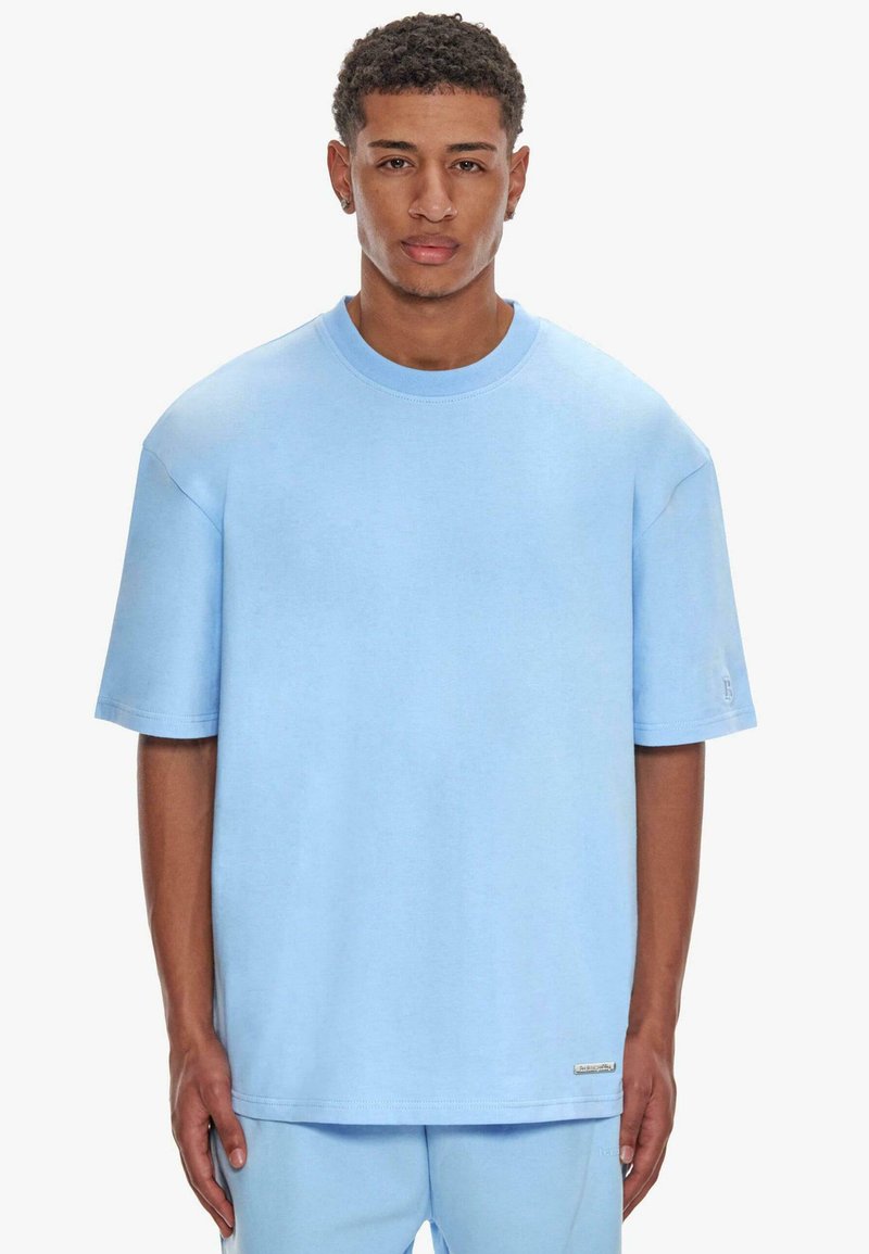 Lyseblå oversized t-shirt i blød bomuld, med korte ærmer, rund hals og diskrete logo-detaljer ved sømmen og ærmet.