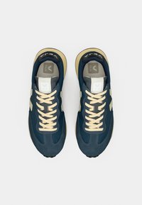 Αθλητικά παπούτσια σε ναυτικό μπλε με μπεζ λεπτομέρειες, διαθέτουν υφή φινιρίσματος, αντίθετα κορδόνια και στρογγυλή μύτη. Λογότυπο στη γλώσσα.
