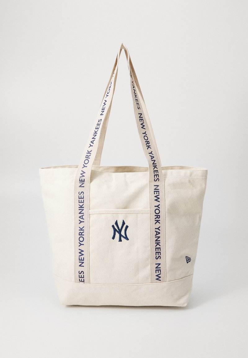 Canvas-Tragetasche in natürlicher Farbe mit marineblauen Nähten. Verfügt über eine Fronttasche und den Text "NEW YORK YANKEES" entlang der Tragen.