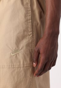 Béžové šortky Nike s hladkou texturou, boční kapsou a vyšitým logem ve stejné barvě na levé noze.