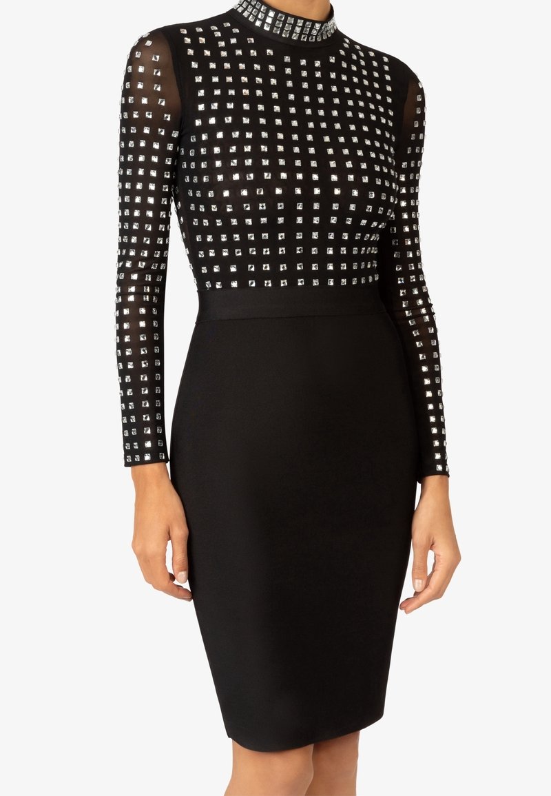 Robe noire moulante avec manches longues transparentes et haut orné de petits clous carrés argentés disposés en motif quadrillé.