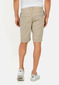 Beige shorts van lichte stof, met twee achterzakken en een omgeslagen zoom. Gemaakt met witte sneakers, gezien vanaf de achterkant.