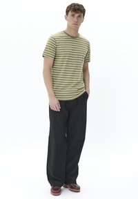 Camiseta de rayas verde olivo con mangas cortas, combinada con pantalones anchos negros y zuecos marrones con suela texturizada.