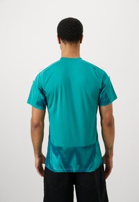 Camisola atlética em verde-água com um design ajustado, mangas curtas, riscas brancas nos ombros e painel inferior texturizado. Tecido suave com propriedades de absorção de humedad.