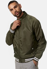 Giacca bomber verde oliva con zip frontale, polsini a coste bianchi e verdi a righe e tasche laterali. Tessuto liscio e leggero.