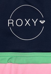 Marineblaue Stoff mit einem weißen "ROXY"-Logo in einem Kreis; darunter, ein grüner und pinker horizontaler Streifen aus glattem, dehnbarem Material.
