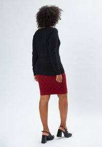 Maglietta nera a maniche lunghe abbinata a una gonna rossa con motivo a rombi. Footwear in sandali neri con tacco largo. Design semplice e aderente.