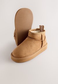 Stivaletti alla caviglia in camoscio color cognac con suola in gomma texturizzata. Presentano una fodera morbida e un cinturino decorativo sul retro per una facile calzata.