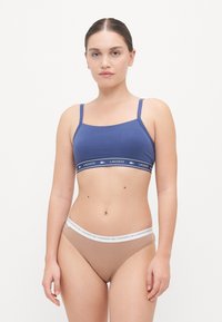 Blå bomullsbralette med tynne stropper og et bånd med Lacoste-logo; beige bomullsboxer med et hvitt bånd som også viser logoen.