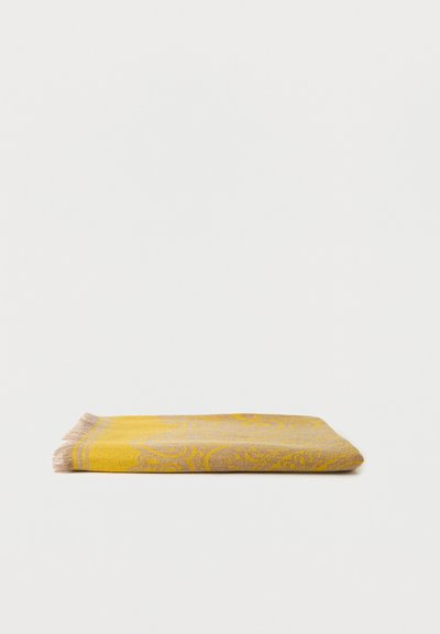 Tissu plié jaune et beige à motifs avec des bords à franges sur un fond blanc uni.