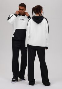 Sweatshirts à capuche noirs et blancs avec une poche avant ; pantalon noir assorti ; tissu lisse ; logo sur la poitrine ; design à coupe décontractée.