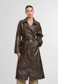 Brązowy płaszcz trench z sztucznej skóry z paskiem w talii, podwójnymi guzikami i szerokimi klapami. Posiada długie rękawy i dopasowaną sylwetkę.