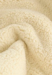 Kermanvärinen fleece-kangas, jossa on tekstuuri ja pörröinen pinta, esittelee pehmeän, aaltoilevan ulkonäön ja tiheän pinnan.