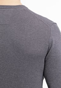 Szary dziergany sweter ukazujący zbliżenie pleców, z prążkowanym dekoltem i subtelną fakturą. Minimalna ilość szwów i klasyczny design.