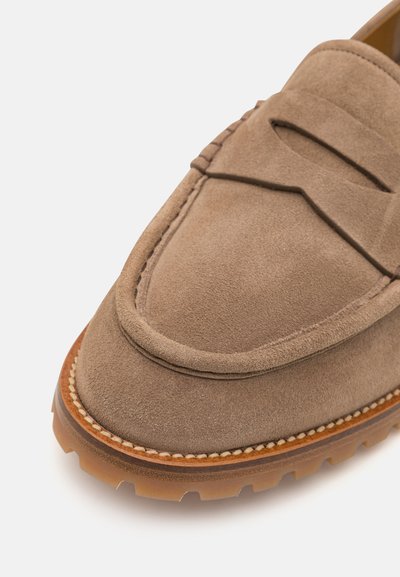 Mocasini din suede maro deschis, cu vârf rotund, cusături decorative și o talpă groasă din cauciuc texturat. Beneficiază de un garnitură din piele contrastantă.